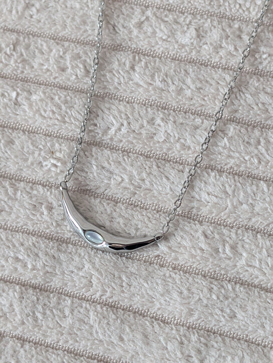 Silver necklace with a moonstone on a textured beige surface